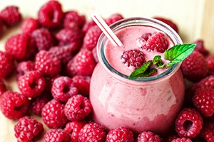 Een tafel gevuld met frambozen met in het midden een glas frambozen smoothie