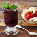 Een tafel met daarop een glas met daarin in acai bessen mouse, een lepel en een schaaltje met wat aardbeien en bananen Een tafel met daarop een glas met daarin in acai bessen mouse, een lepel en een schaaltje met wat aardbeien en bananen