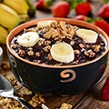Schaaltje met acai yoghurt, een lepel, een aantal bananen en aardbeien Schaaltje met acai yoghurt, een lepel, een aantal bananen en aardbeien