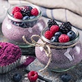 Een grijze tafel met 2 glazen met daarin acai mouse en een schaaltje met paars poeder Een grijze tafel met 2 glazen met daarin acai mouse en een schaaltje met paars poeder