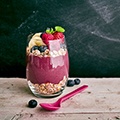 Tafel met een glas acai mouse, granen, bessen en frambozen met daarnaast een lepel Tafel met een glas acai mouse, granen, bessen en frambozen met daarnaast een lepel