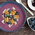 Een kom met acai pap versiert met witte chochola en granen met daarnaast een schaaltje met bessen Een kom met acai pap versiert met witte chochola en granen met daarnaast een schaaltje met bessen