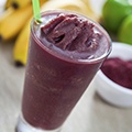 Een glas met acai bessen smoothie en een paar bananen op de achtergrond Een glas met acai bessen smoothie en een paar bananen op de achtergrond
