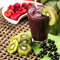 Een tafel met met daarop een gesneden kiwi, een aantal bessen en een glas met een smoothie van acai bessen Een tafel met met daarop een gesneden kiwi, een aantal bessen en een glas met een smoothie van acai bessen