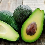 Meerdere avocados bij elkaar waarvan er een door de helft is gesneden en dus de pit te zien is