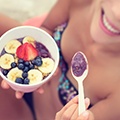 Vrouw in bikini die geniet van een schaaltje acai yoghurt versiert met wat bananen en bessen