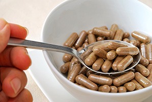 Wit schaaltje met daarin bruine poeder capsules en iemand die deze eet met een lepel Wit schaaltje met daarin bruine poeder capsules en iemand die deze eet met een lepel