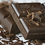 Twee afgebroken stukken pure chocolade met daarnaast wat kleine stukjes chocola