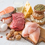 Tafel met daarop allerlei etenswaren zoals kaas, rauw vlees, rauwe kipfilet, rauwe zalm, nootjes, kruiden en eieren