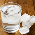 Een tafel met daarop een glas ijskoud water en daarnaast een paar ijsklontjes