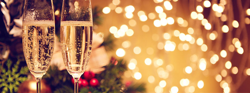 Een tafel met daarop 2 glazen champange en op de achtergrond kerstversiering en kerstlichtjes