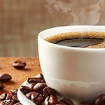 Houte tafel met daarop een wit kopje met koffie en daarnaast wat koffiebonen