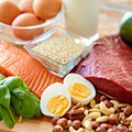 Een tafel met daarop gekookte eieren, zalm, nootjes, vlees, havermout en een glas met melk