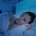 Een vrouw die aan het slapen is in een bed terwijl ze een stuk van haar deken vasthoudt in haar hand
