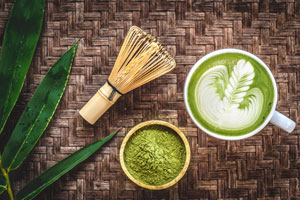 Tafel met een schaaltje matcha poeder, een kopje matcha koffie en een mixstaaf