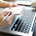 Laptop met daarboven iemand zijn hande die een notitieboekje en een pen vastheeft - onderzoek