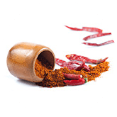 Een neergelegd potje met eruit rood peper poeder, een rode peper en wat schillen van rode pepers