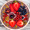 Roze schaaltje met daarin roze yoghurt versierd met fruit zoals aardbeien, blauwe bessen en granen