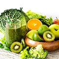 Een schaal vol met fruit zoals kiwi, appel, sinnaasappel en glas met groen sap