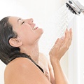 Een vrouw onder de douche, met haar gezicht richting de douchekop en haar handen in een kommetje