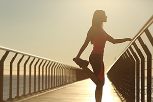 Vrouw die alleen op een brug staat en een sportoefening doet waarbij ze een van haar voeten via achter vast heeft