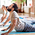 Een man met een donkere baard bij een yoga-les die op zijn buik ligt en zijn bovenlichaam naar boven duwt